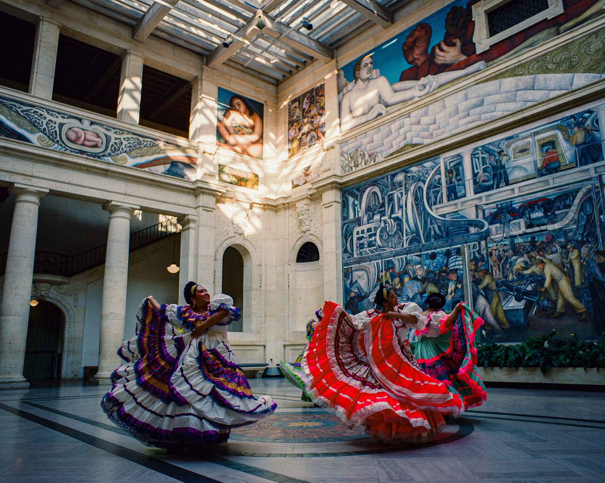 Folklórico dancers in a mural-lined hall