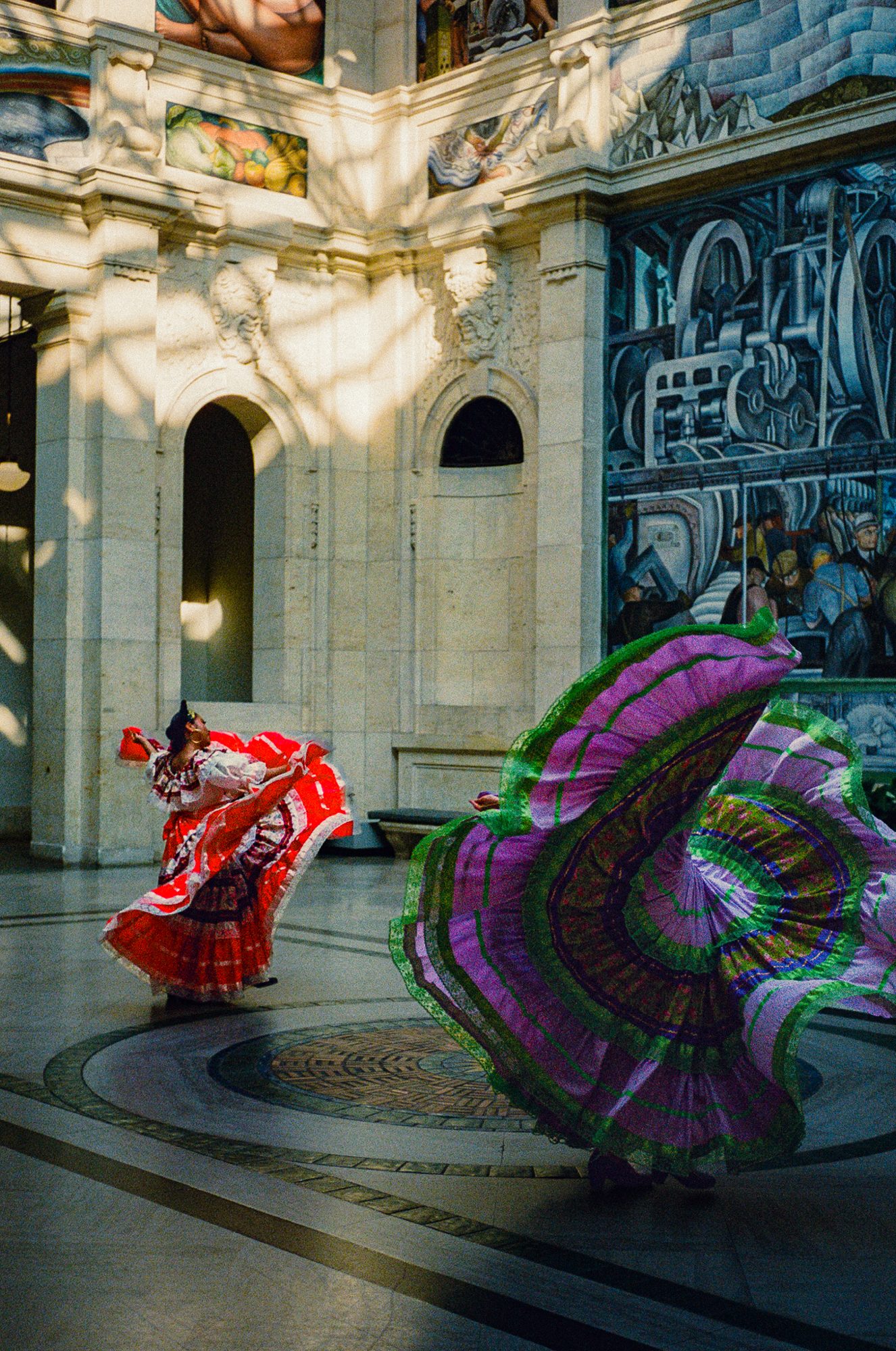Dancers spinning in a mural-lined hall